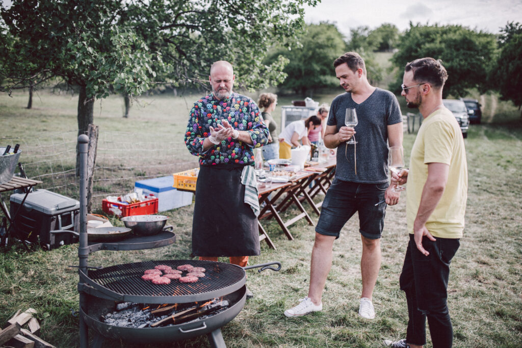 Three people standing at a grill where hamburgers are being fried