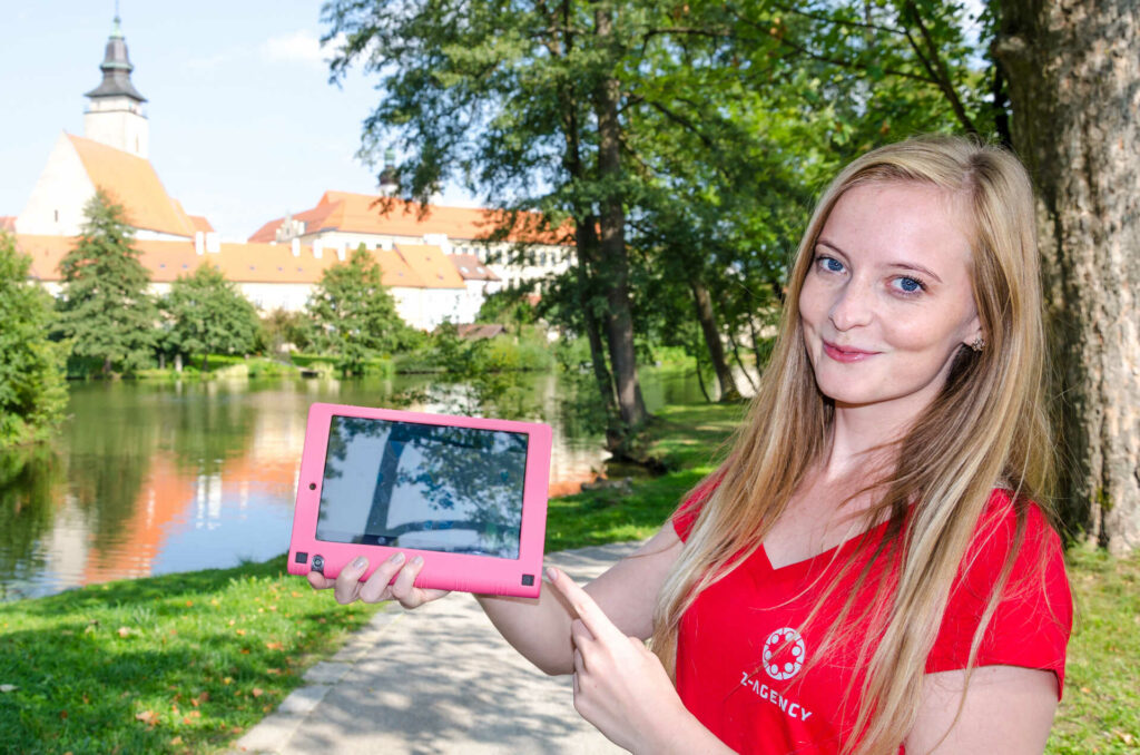 a lady in a red t-shirt holding a pink tablet in one hand and pointing at it with the other hand